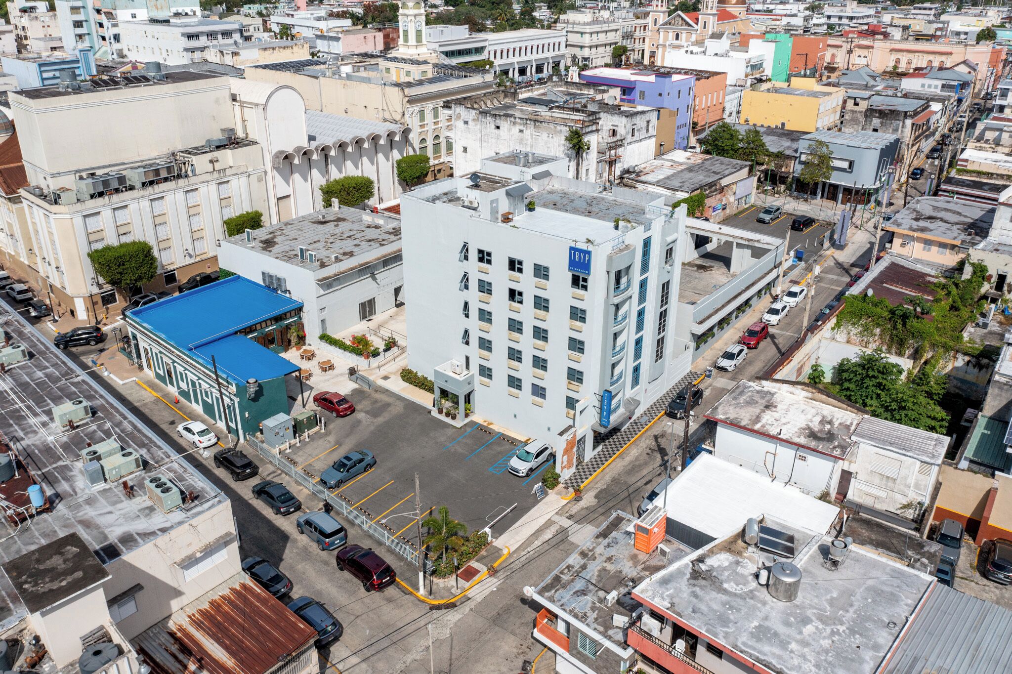 A multi-story building with a blue roof, parking lot, and several vehicles.