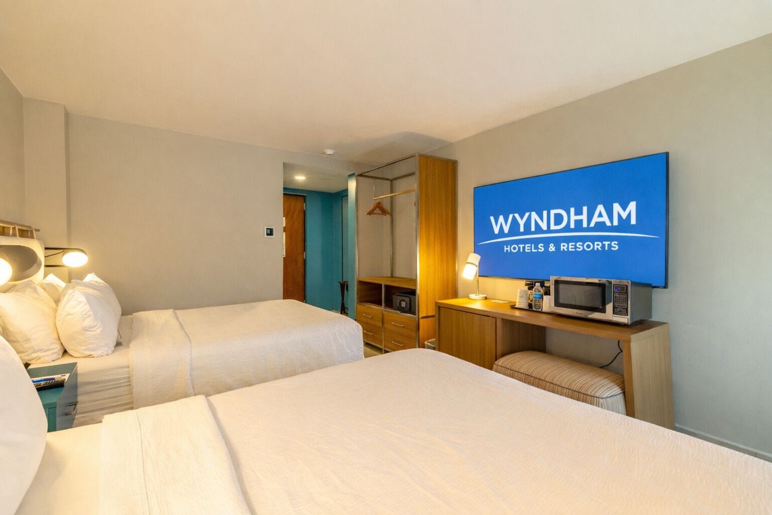 Una habitación de hotel con dos camas, un televisor, un escritorio con microondas y un armario.