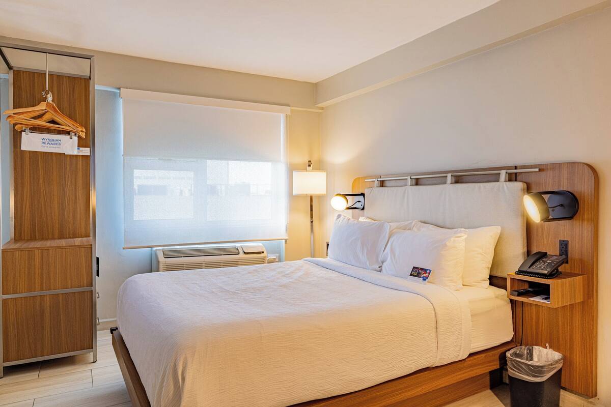A hotel room with a bed, bedside lamp, phone, and a hanging garment rack.
