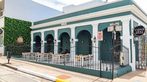 Un bâtiment à la façade verdoyante, portant le numéro 1866, doté d’une terrasse avec des chaises et des tables, d’une entrée fermée par un portail et d’une enseigne indiquant le restaurant « Casa Abu ».