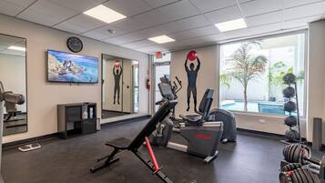 A gym with exercise equipment, a large mirror, a clock, and a painting of a rocky coastline.