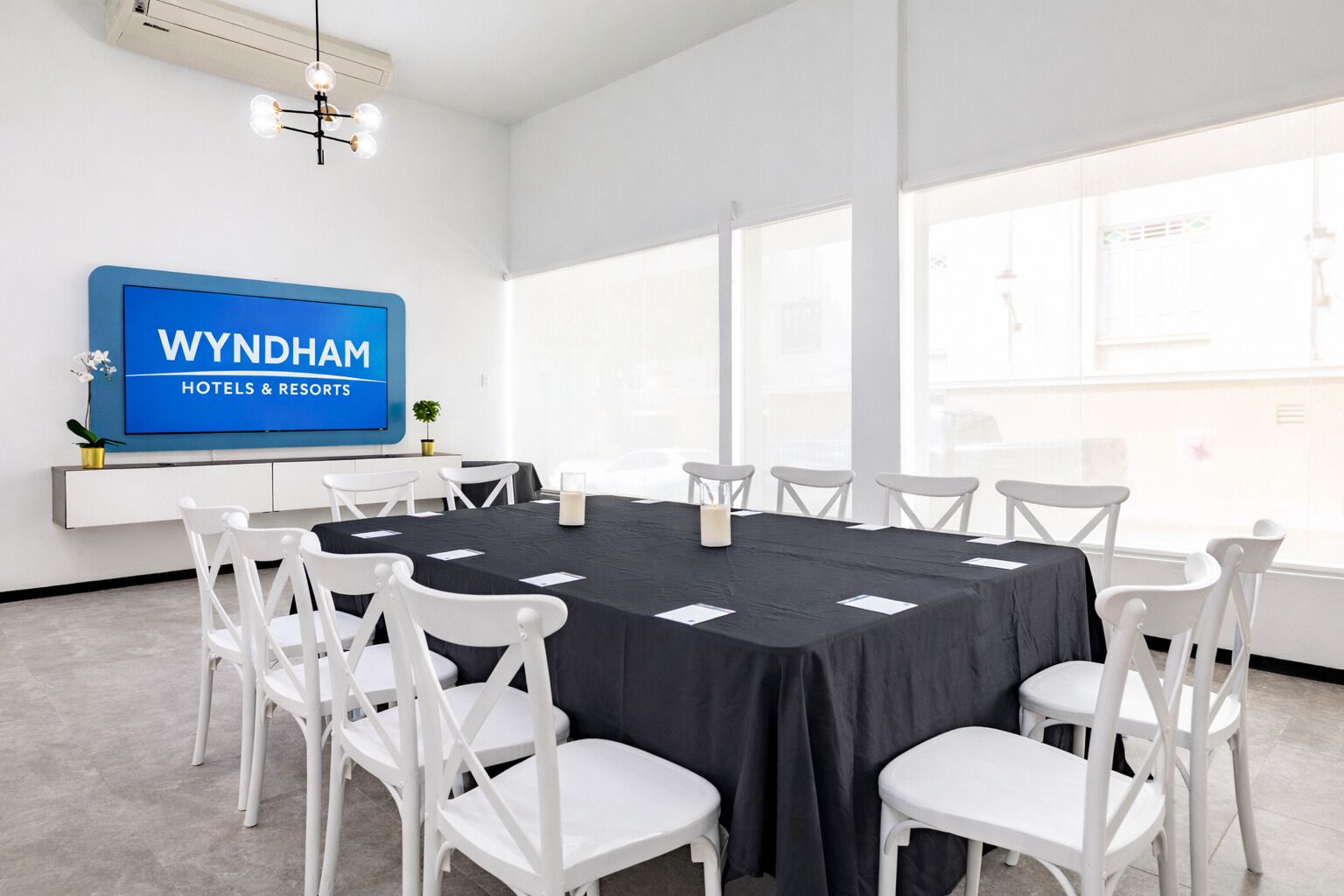 Une salle de conférence avec une table noire, des chaises blanches, un panneau bleu et de grandes fenêtres.