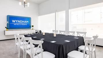 Une salle de conférence avec une table noire, des chaises blanches, un panneau bleu et de grandes fenêtres.