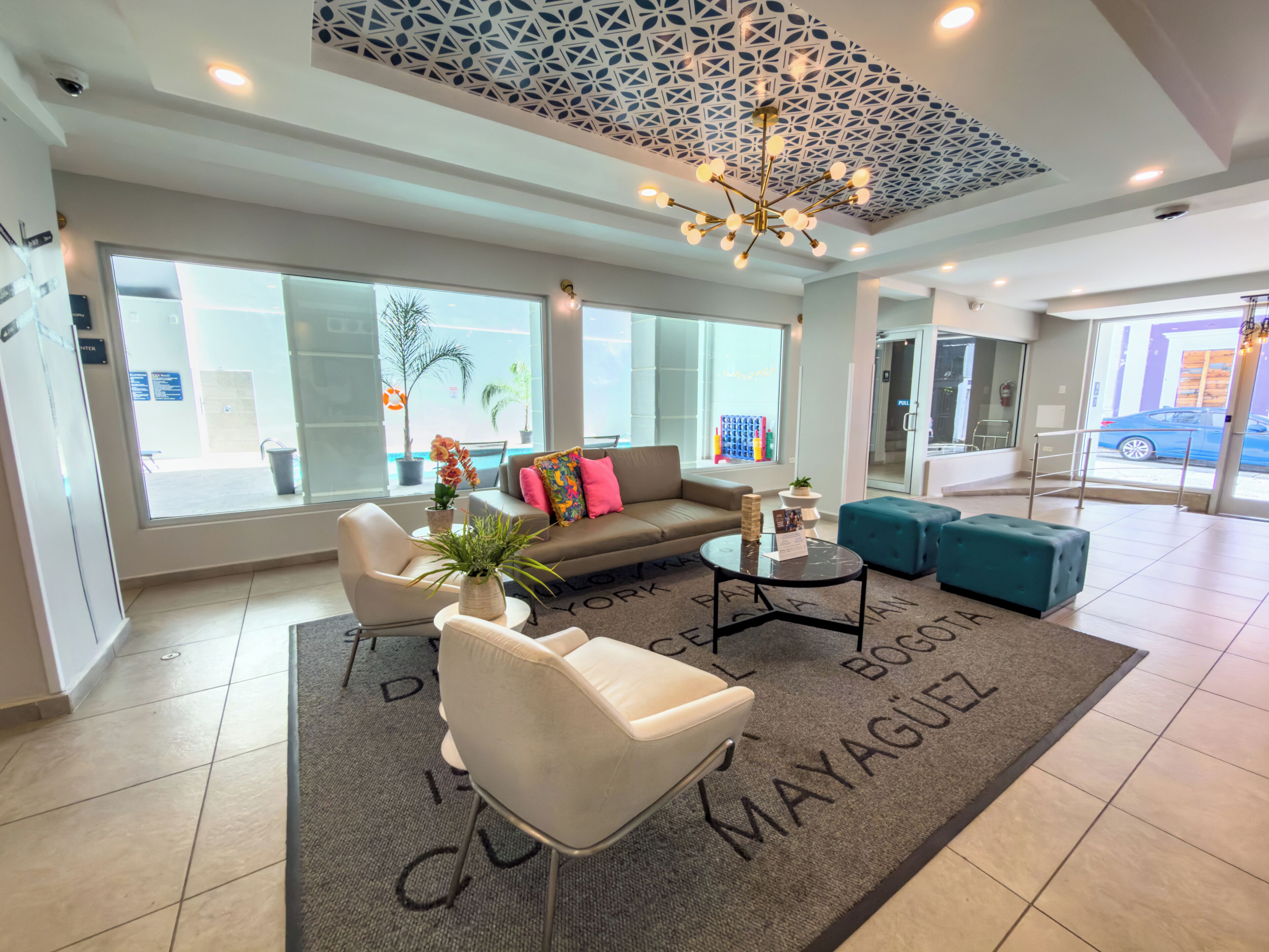 A modern hotel lobby with a sofa, chairs, a chandelier, and a large window.