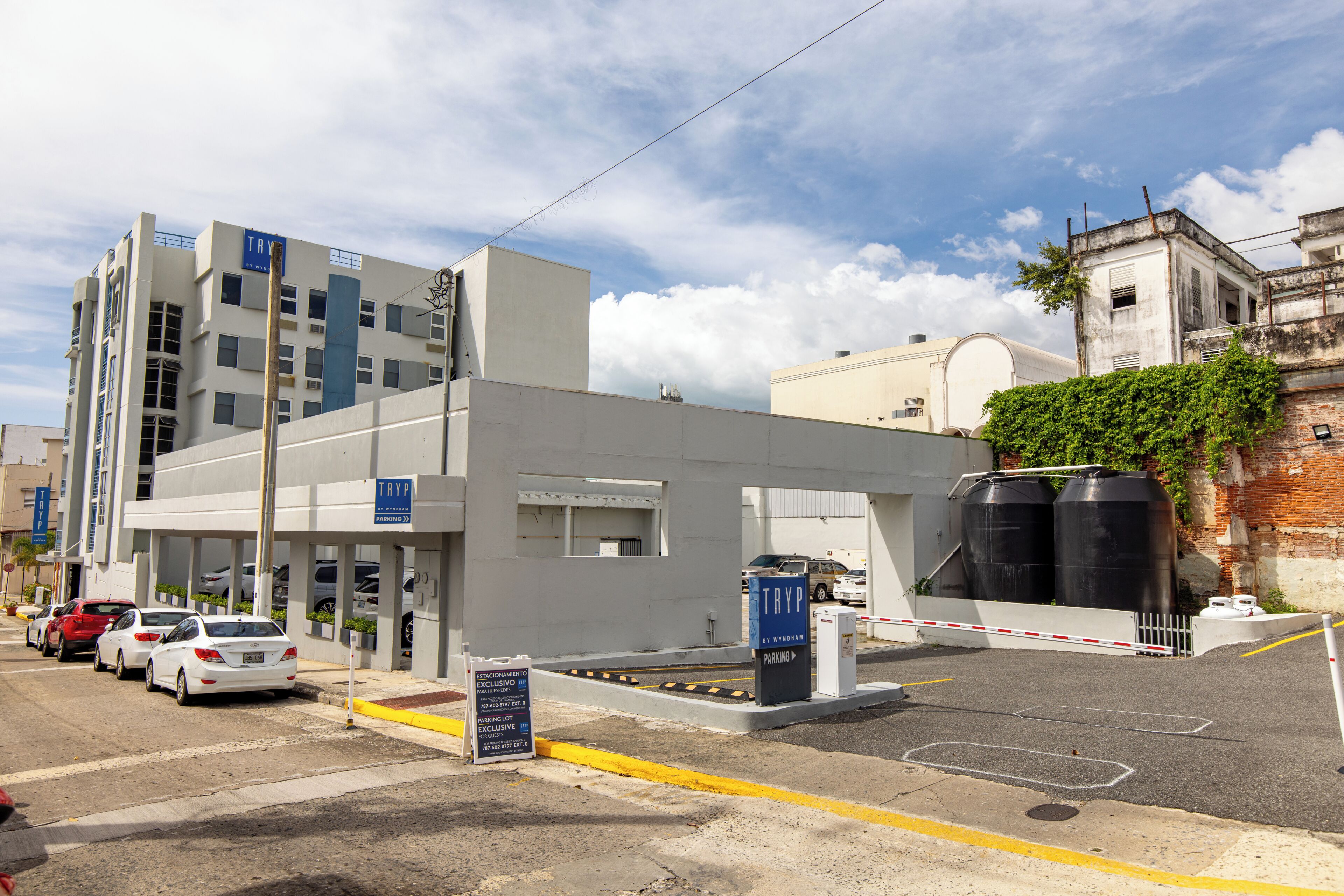 A parking lot with a gated entrance, a building with a sign, and several parked cars.