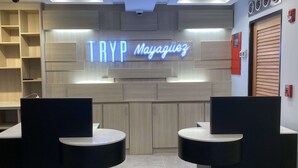 Un espace d’accueil avec un panneau néon indiquant « TRYP Mayaguez », deux comptoirs d’accueil noirs, un lambris en bois et un détecteur d’incendie mural.