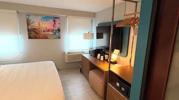 A hotel room with a bed, a desk with a computer, a TV, and a painting on the wall.