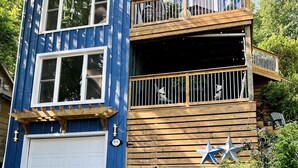 Een tweelaags huis met een blauwe gevel, een witte garage deur en een houten terras met een hekwerk.