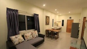 Ein Wohnzimmer mit einer Couch, einem Esstisch mit Stühlen, einem Fernseher und einem Kühlschrank.
