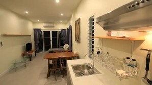 Eine kompakte Küche mit Spüle, ein Essbereich mit Stühlen, einem Fernseher und einem Fenster mit Vorhängen.