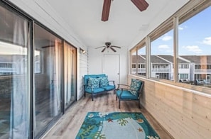 Relax on the balcony with a view of the surrounding neighborhood, featuring a comfortable seating area with a ceiling fan.