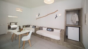 Een moderne, minimalistische kamer met een eettafel, witte stoelen, een bank met kussens in de vorm van ogen, een kleine koelkast en een decoratieve tak aan de muur.