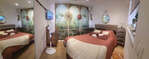 A hotel room with two beds, a large mirror, a wall-mounted TV, and a decorative sunburst mirror.