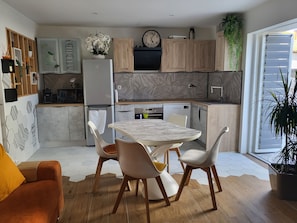 A modern kitchen with a dining area, featuring a marble table, white chairs, and a wooden floor.