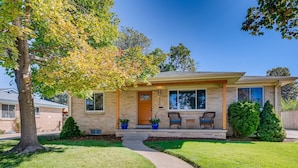 A two-story house with a brick facade, a front porch with two chairs, and a small tree to the left. - Well-Appointed Family Summer Home - King Bed - Close to DEN & Anschutz (Aurora)