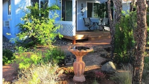 A blue house with a covered porch, a stone fountain, and a garden with various plants and trees.