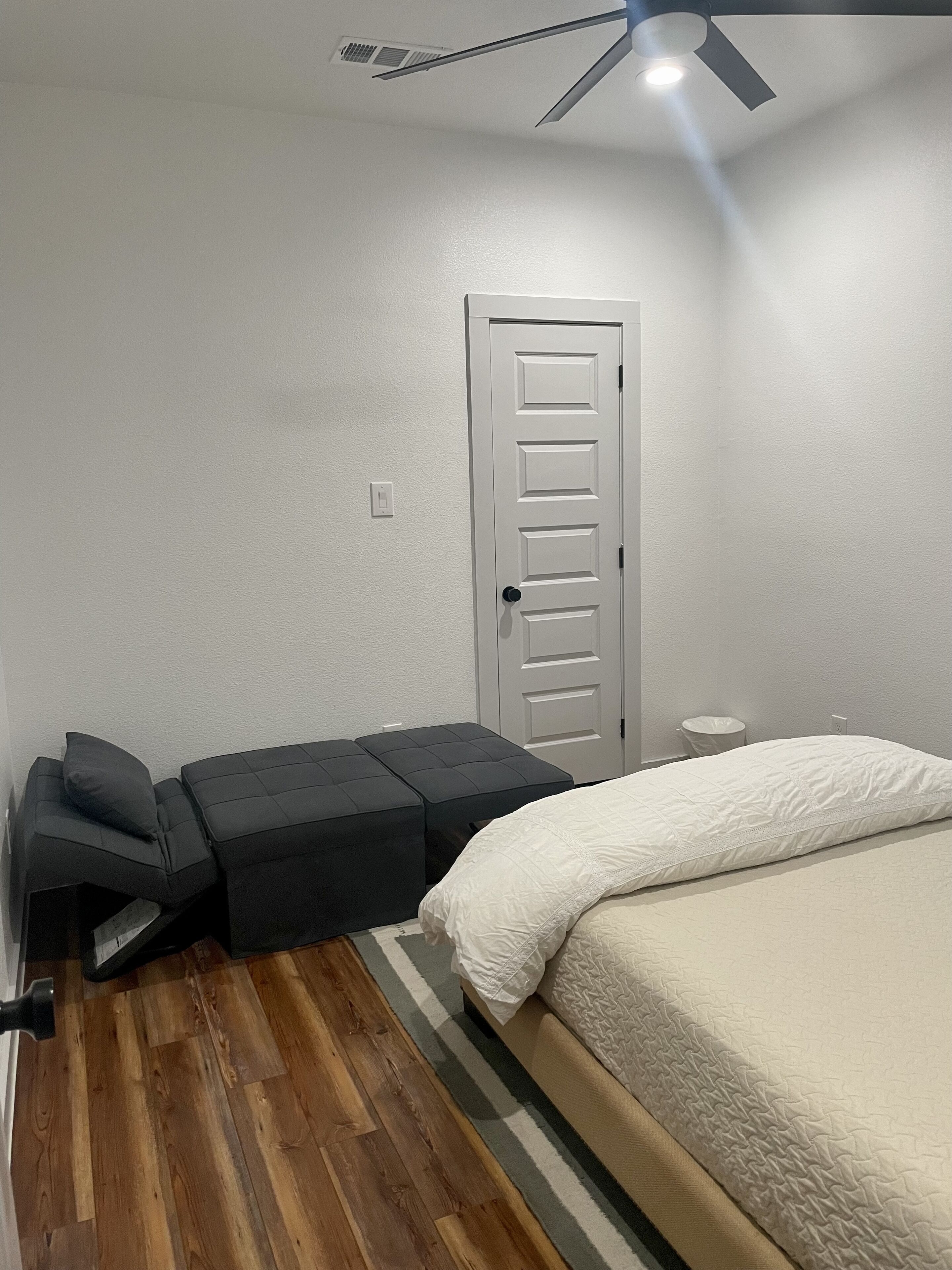Une chambre à coucher avec un lit, un ventilateur de plafond, une porte et une petite table avec un coussin.
