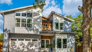 Uma casa moderna de dois andares com garagem, gramado bem cuidado e uma grande árvore em primeiro plano.