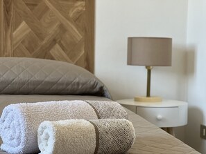 A neatly made bed with rolled towels, a wooden headboard, a bedside lamp, and a white nightstand. - Apartment in Porto Frailis (Arbatax)