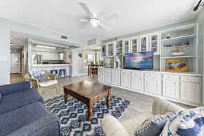 A spacious living room with a large TV, white cabinetry, and a ceiling fan. - Compass Point 310 (Gulf Shores)