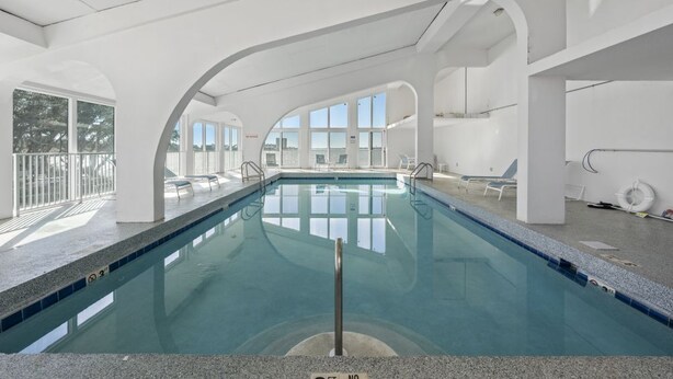 An indoor swimming pool with clear glass walls, a tiled floor, and a no diving sign. - Compass Point 310 (Gulf Shores)