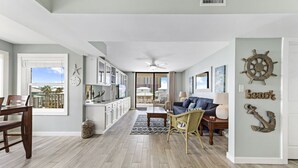 A spacious living area with a dining table, a sofa, and a kitchen in the background. - Compass Point 310 (Gulf Shores)