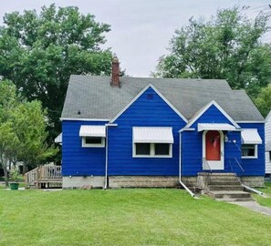 Una casa azul con puerta roja, contraventanas blancas y una chimenea.