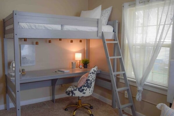 Una cama litera con escritorio y silla, una escalera, una lámpara y una ventana con cortinas.
