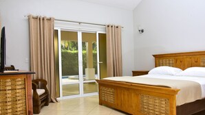 Une chambre avec un lit en bois, une petite table en bois, une chaise et une porte-fenêtre coulissante donnant sur un balcon.