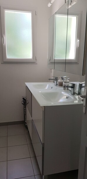 Une salle de bain moderne avec deux lavabos, un grand miroir et des fenêtres en verre dépoli.