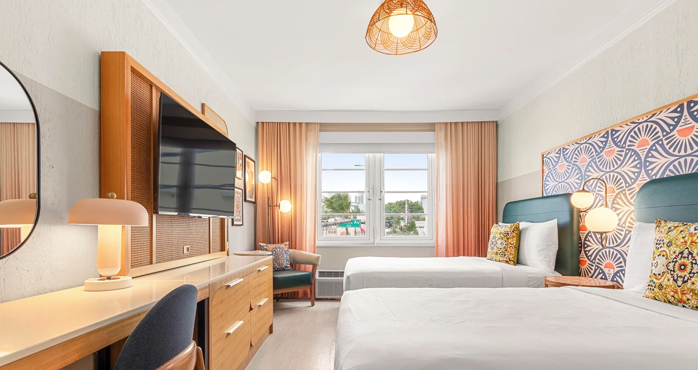 Hotelkamer met een bed, een bureau met televisie, een stoel, een raam met gordijnen en een kamerhordings.