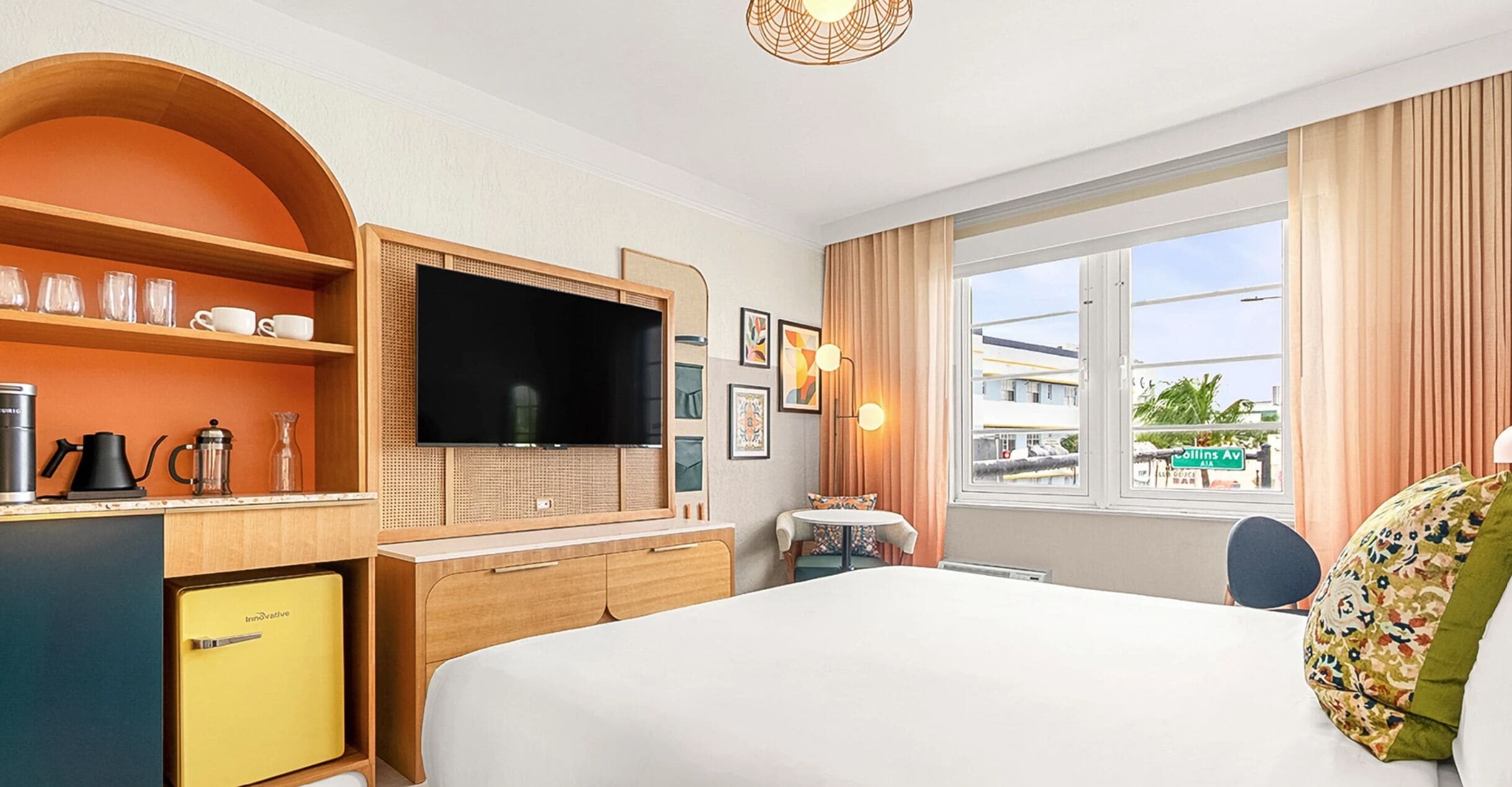Een hotelkamer met een bed, een televisie, een bureau met stoel, een raam met gordijnen en een kitchenette.