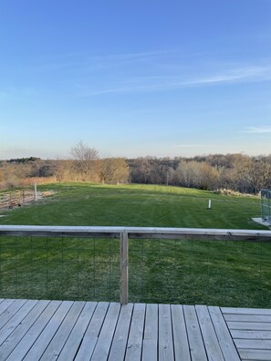 Eine Holzterrasse mit Blick auf ein Wiesenfeld und Bäume in der Ferne.
