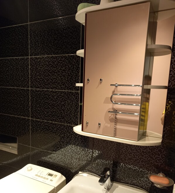 A bathroom with a large mirror, a sink, and a shower area. - Dviejų kambarių butas su vaizdu į baseiną (Palanga)