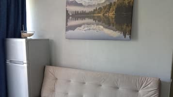 Una sala de estar moderna con un sofá color beige, un refrigerador y un cuadro con un paisaje en la pared.
