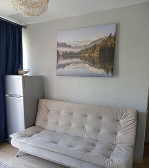 Una sala de estar moderna con un sofá color beige, un refrigerador y un cuadro con un paisaje en la pared.