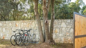 Eine Steinmauer mit einem hölzernen Tor, zwei Fahrräder sind dagegen abgestellt, und Bäume sind im Hintergrund zu sehen.