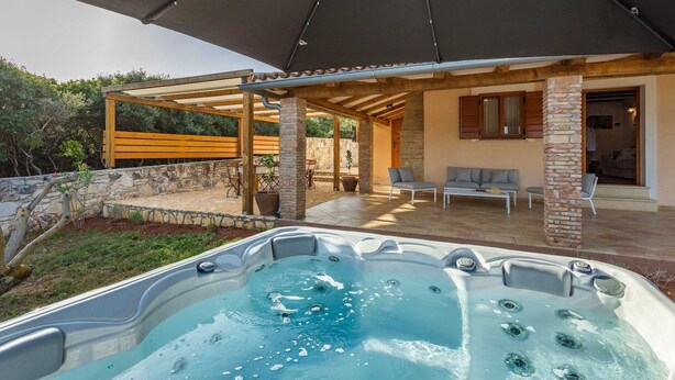 Ein Whirlpool unter einer überdachten Terrasse mit Steinwänden und Holzmöbeln.