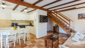 Eine Küche mit weißen Schränken, einem Esstisch mit Stühlen, einer Holztreppe und einem Wohnbereich mit einer Couch und einem Couchtisch.