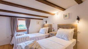 Ein Schlafzimmer mit zwei Betten, Holzbalken an der Decke, einem Fenster mit Vorhängen und einem Nachttisch mit Lampe.