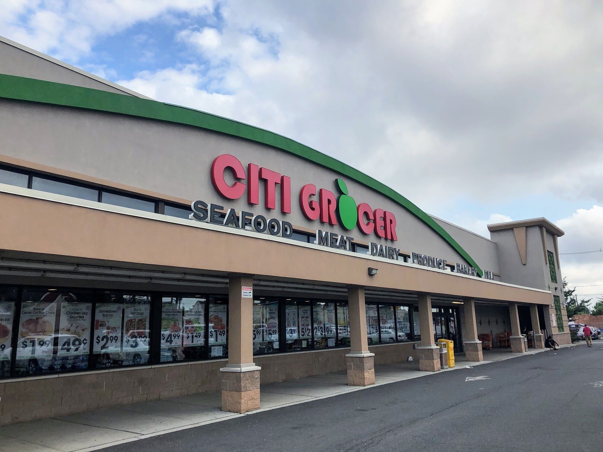 Una tienda CITI GROCER con techo verde y grandes ventanales que exhiben precios de mariscos y carne.