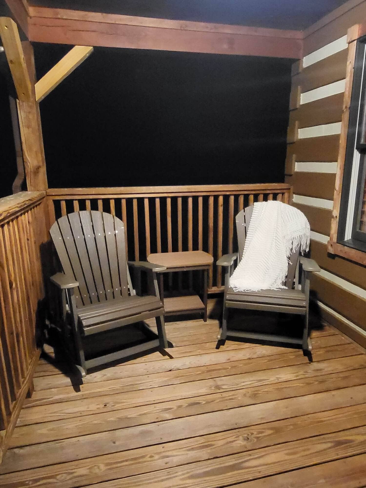 Een houten terras met twee Adirondack-stoelen en een kleine tafel, omgeven door houten balustrades.