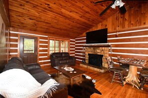 A log cabin interior with a fireplace, leather sofa, dining table, and a mounted television. - Lakeshore Retreat (Abingdon)