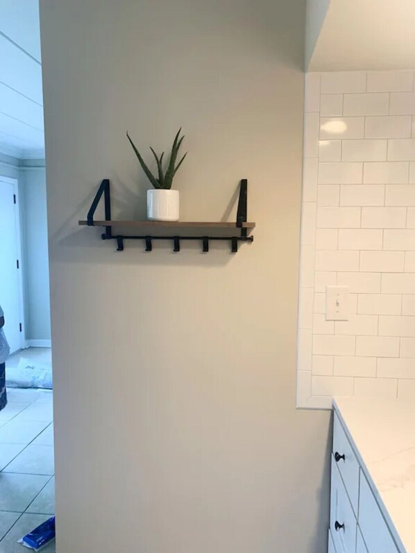 A kitchen with a white tiled backsplash, a wooden shelf with a potted plant, and a white cabinet with drawers.