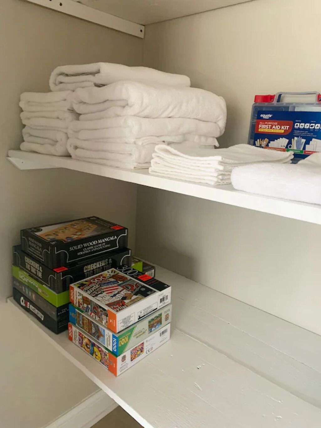 Uno spazio di stoccaggio con scaffali che contengono asciugamani bianchi piegati, un kit di pronto soccorso e diversi giochi da tavolo.