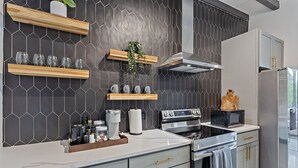 Cozinha moderna com painel de azulejos hexagonais, prateleiras de madeira, forno embutido e geladeira de aço inoxidável.
