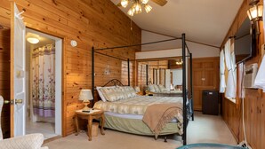 A four-poster bed with a canopy, a wooden floor, a small table with a lamp, a chair, and a television mounted on the wall. - One-of-a-kind 4 Acre Adirondack Escape Short Drive to LG & GORE Mountain!
 (Warrensburg)