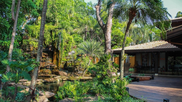 A serene garden with a pond, lush greenery, and a wooden deck with outdoor seating. - Pobore Pousada Spa Gastronomia (Rondonopolis)