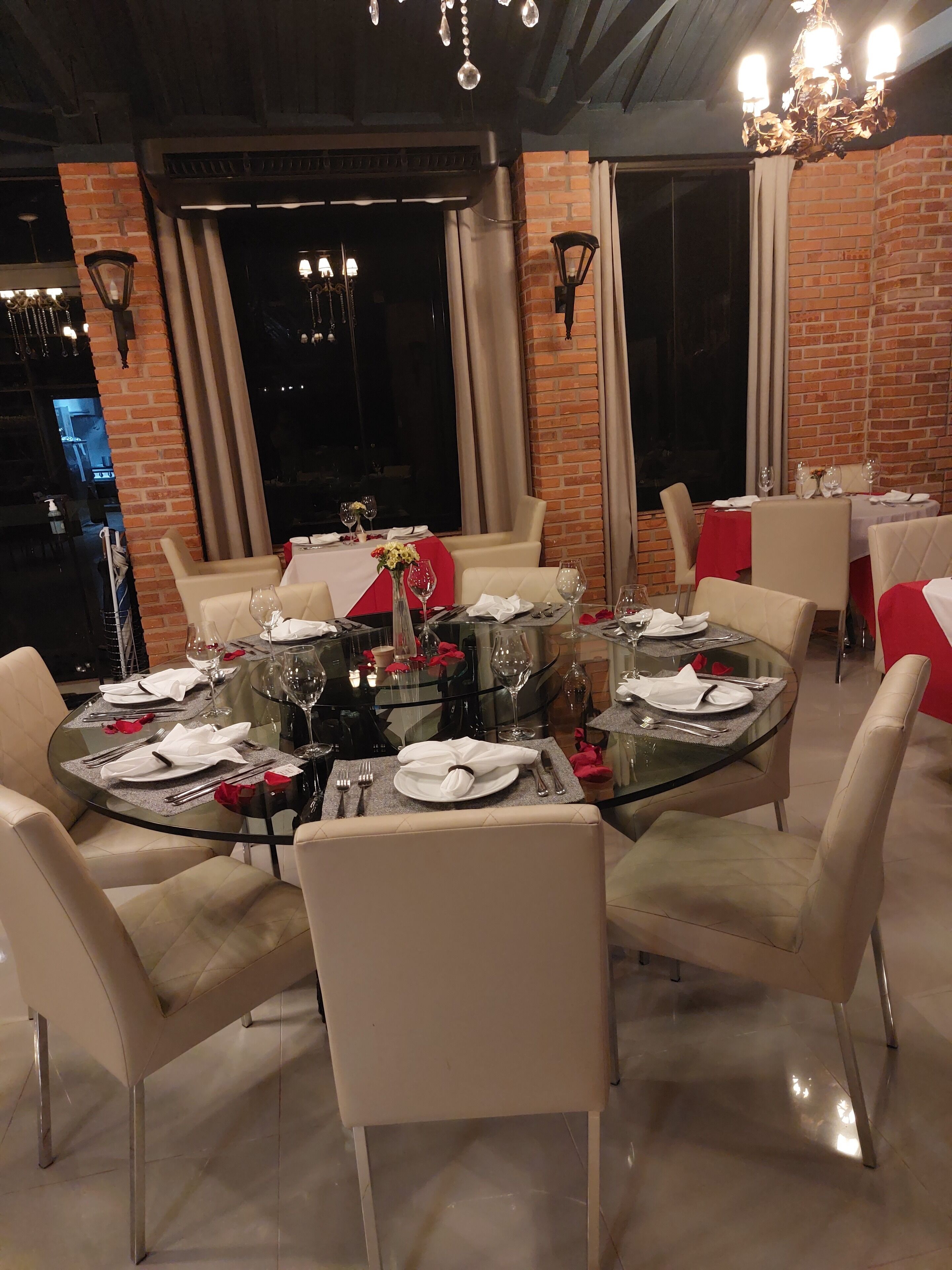 A restaurant with round glass tables, white chairs, and brick walls.