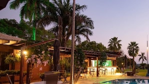 A poolside area with a pool, lounge chairs, and a building with outdoor seating. - Pobore Pousada Spa Gastronomia (Rondonopolis)